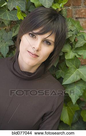 Picture - Hispanic woman leaning on ivy-covered wall. Fotosearch