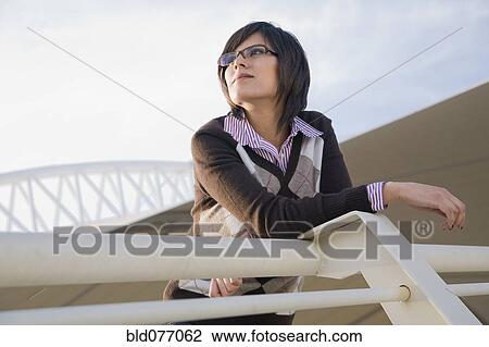 Stock Image - Hispanic woman leaning on urban railing. Fotosearch