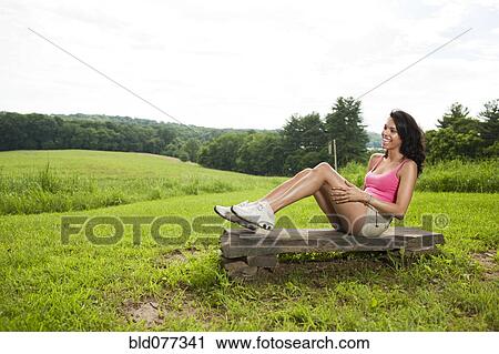 Stock Image - Hispanic woman sitting on rock in field. Fotosearch