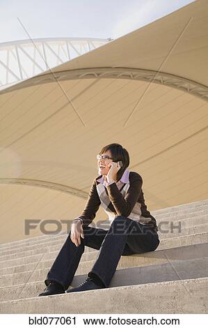 Stock Image - Hispanic woman talking on cell phone on steps. Fotosearch