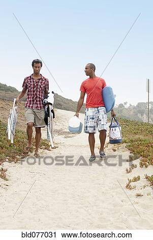 Stock Image - Men carrying cooler, chairs and bags to beach. Fotosearch