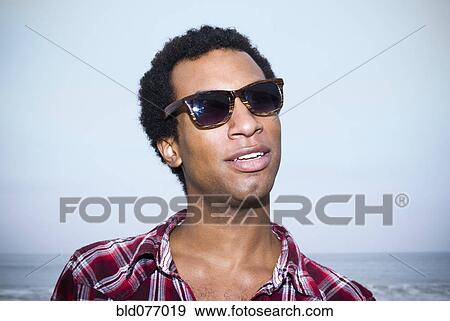 Stock Photo - Mixed race man in sunglasses at ocean. Fotosearch