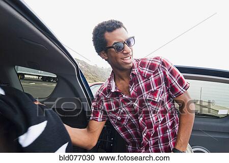 Stock Image - Mixed race man removing blanket from back of car. Fotosearch