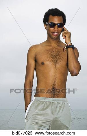 Stock Image - Mixed race man talking on cell phone at ocean. Fotosearch