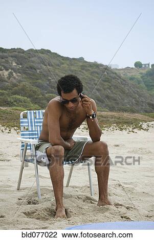 Stock Image - Mixed race man talking on cell phone on beach. Fotosearch