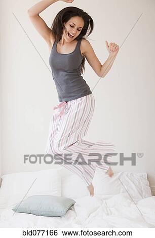 Stock Photograph - Mixed race woman jumping on bed. Fotosearch