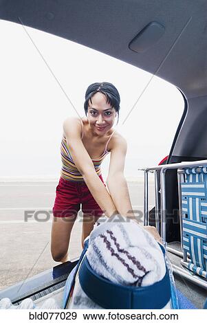 Stock Photo - Mixed race woman removing bag from car at beach. Fotosearch