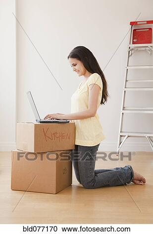 Stock Image - Mixed race woman using laptop on cardboard boxes. Fotosearch