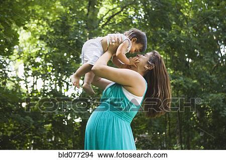 Picture - Pregnant Hispanic woman lifting baby boy. Fotosearch
