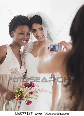 Stock Photo - Woman taking picture of bride and bridesmaid. Fotosearch