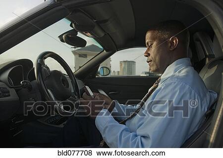 Stock Photo - African businessman in car text messaging on cell phone. Fotosearch