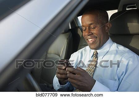 Stock Photo - African businessman in car text messaging on cell phone. Fotosearch