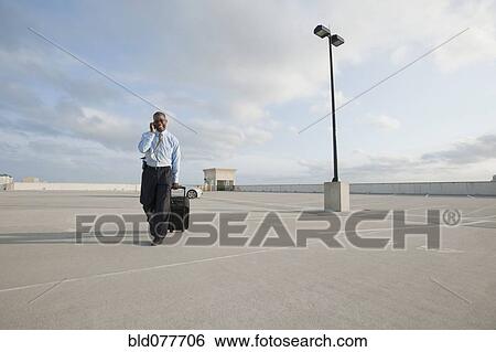 Stock Photograph - African businessman pulling luggage in parking lot. Fotosearch