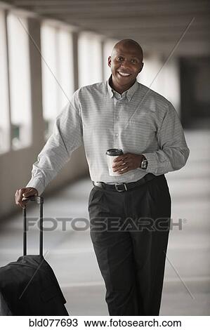 Stock Image - African businessman standing in parking garage with luggage. Fotosearch