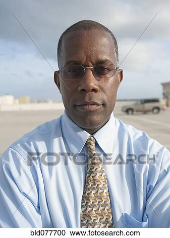 Stock Image - African businessman standing in parking lot. Fotosearch