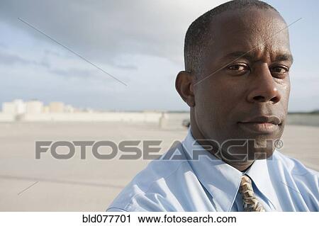 Stock Image - African businessman standing in parking lot. Fotosearch