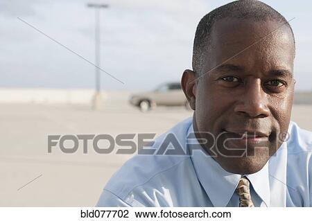 Stock Image - African businessman standing in parking lot. Fotosearch