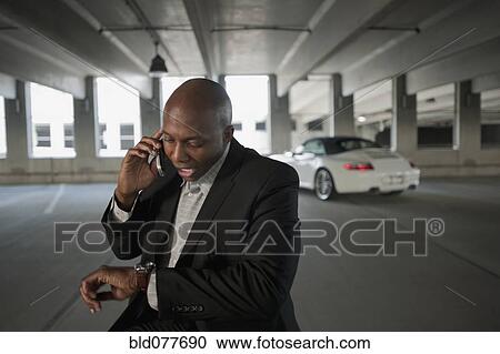 Stock Image - African businessman talking on cell phone in parking garage. Fotosearch