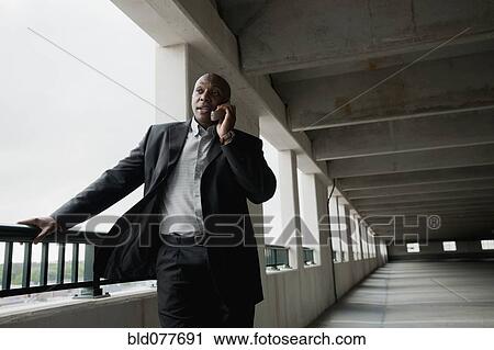 Stock Image - African businessman talking on cell phone in parking garage. Fotosearch