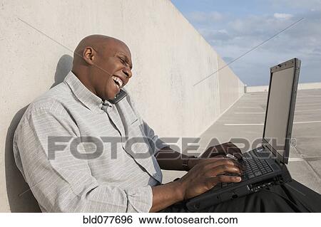 Stock Photograph - African businessman using laptop in parking lot. Fotosearch