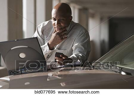 Stock Photography - African businessman using laptop on car hood. Fotosearch