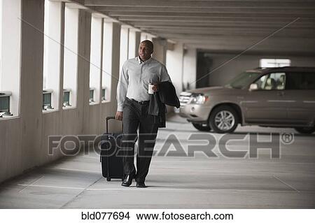 Picture - African businessman walking in parking garage with luggage. Fotosearch