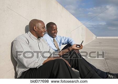 African businessmen looking at cell phone in parking lot View Large Photo Image Stock Photo - African businessmen looking at cell phone in parking lot. Fotosearch