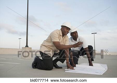 Picture - African businessmen looking at blueprints in parking lot. Fotosearch