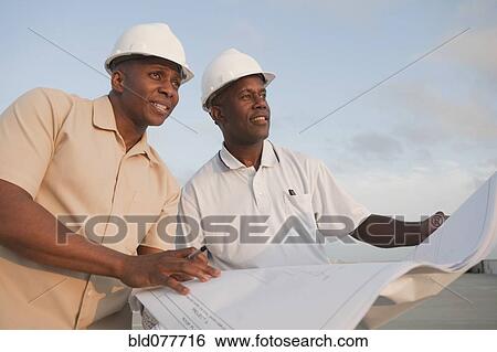 Stock Photograph - African businessmen looking at blueprints in parking lot. Fotosearch