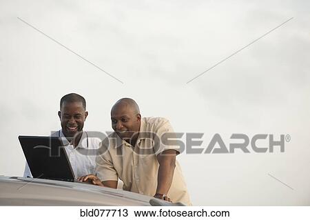 Stock Image - African businessmen using laptop on car hood. Fotosearch