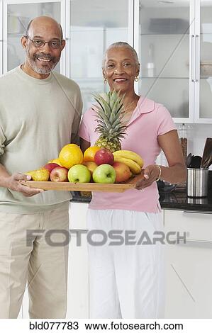 Stock Image - African couple holding tray of fruit. Fotosearch