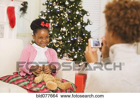 Picture - African mother taking picture of daughter at Christmas. Fotosearch