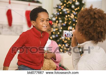 Stock Photo - African mother taking picture of son at Christmas. Fotosearch
