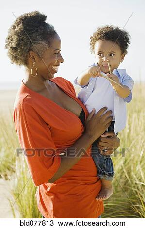 Stock Image - African woman holding son at beach. Fotosearch