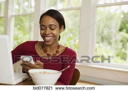 Stock Image - African woman reading text message at breakfast. Fotosearch