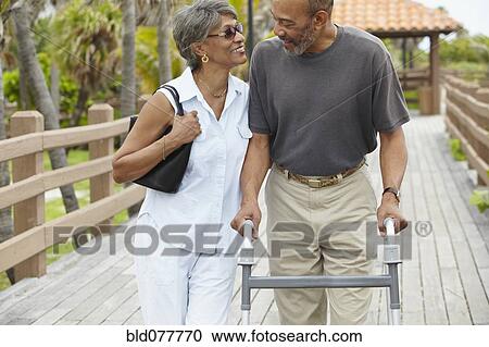 Stock Image - African woman walking with husband using walker. Fotosearch
