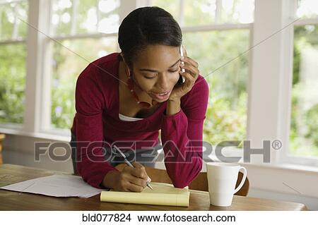 Picture - African woman writing and talking on cell phone. Fotosearch