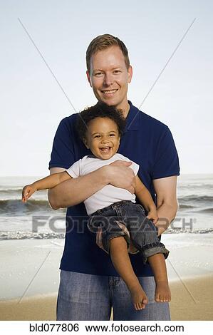 Stock Photograph - Father holding mixed race son at beach. Fotosearch