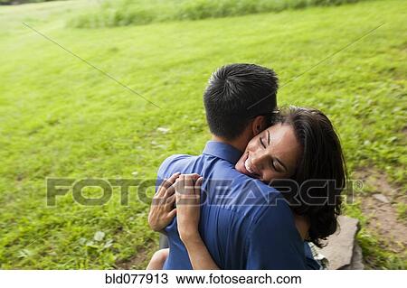 Stock Image - Hispanic couple hugging in field. Fotosearch