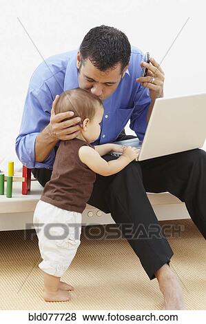 Stock Photo - Hispanic father kissing daughter and using laptop. Fotosearch