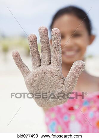 Stock Photo - Hispanic girl displaying sand-covered hand. Fotosearch
