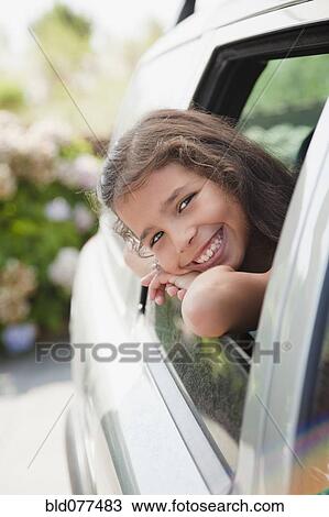 Stock Image - Hispanic girl smiling out car window. Fotosearch