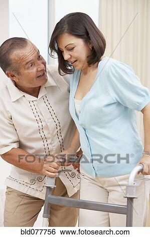 Stock Photograph - Hispanic man encouraging wife using walker. Fotosearch