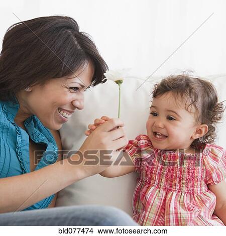 Picture - Hispanic mother handing daughter flower. Fotosearch
