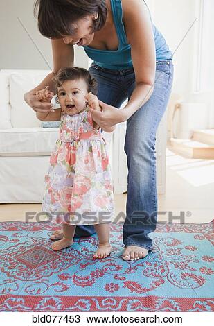 Stock Image - Hispanic mother helping daughter learn to walk. Fotosearch