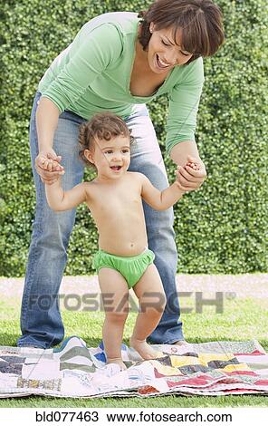 Stock Image - Hispanic mother helping daughter learn to walk. Fotosearch