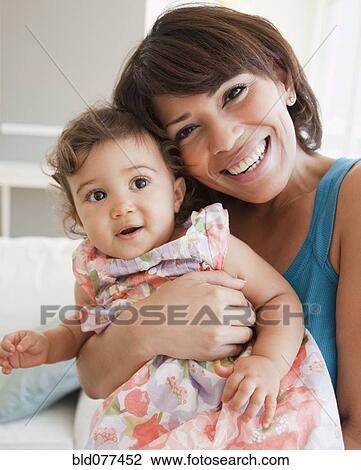 Stock Image - Hispanic mother holding baby girl. Fotosearch