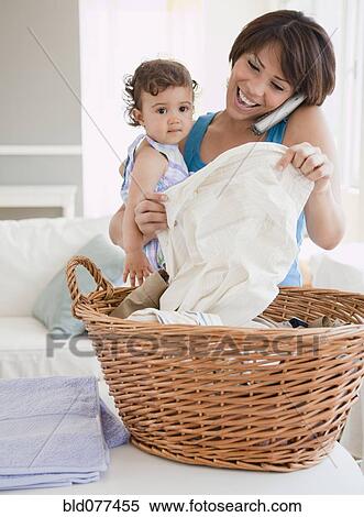 Hispanic mother holding daughter, talking on phone and doing laundry View Large Photo Image Stock Photography - Hispanic mother holding daughter, talking on phone and doing laundry. Fotosearch