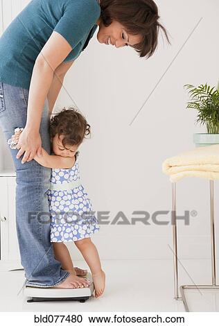 Stock Image - Hispanic mother weighing herself and daughter. Fotosearch