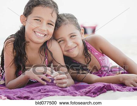 Stock Image - Hispanic sisters relaxing on towel at beach. Fotosearch